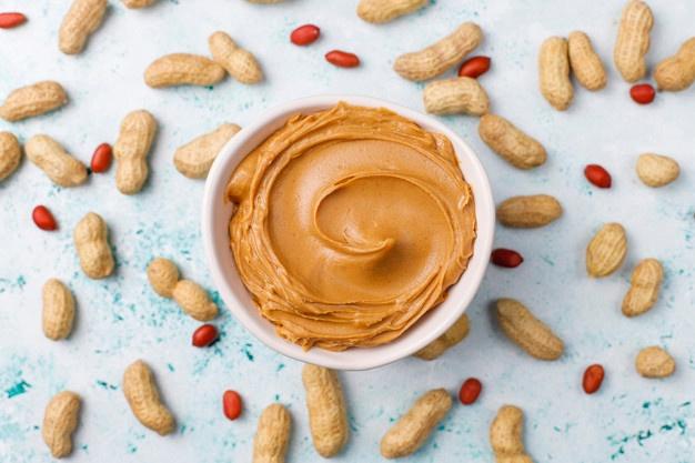 Peanut butter in a bowl surrounded by whole peanuts